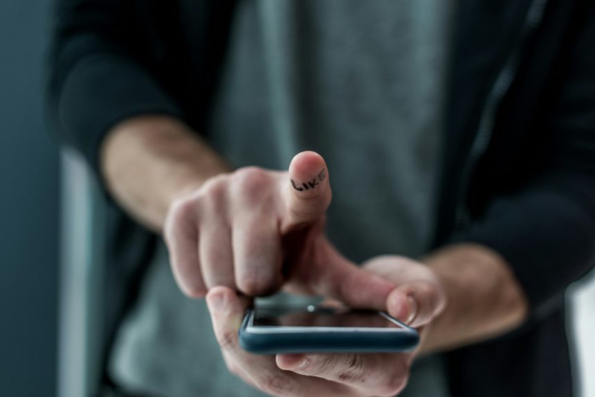 cropped shot of man touching smartphone screen with like sign on finger, phone addiction concept