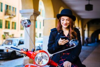 Italy, Verona, young woman with scooter looking at cell phone