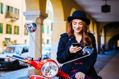 Italy, Verona, young woman with scooter looking at cell phone