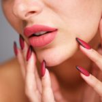 partial portrait of woman with red manicure and flawless complexion