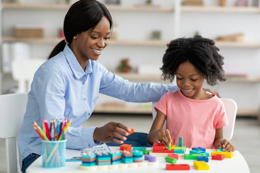 Pretty black kid and child development specialist playing with bricks